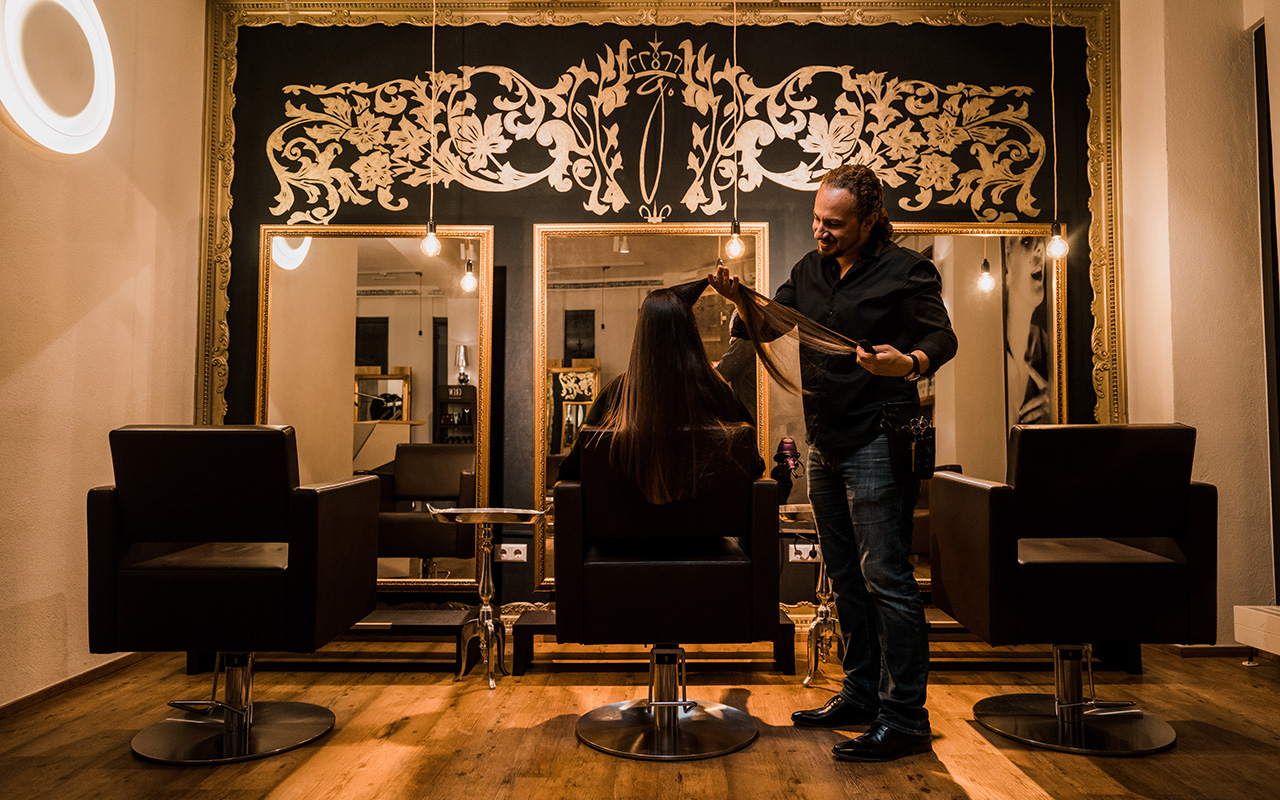 Ein Friseur schneidet im Salon die Haare einer Kundin.